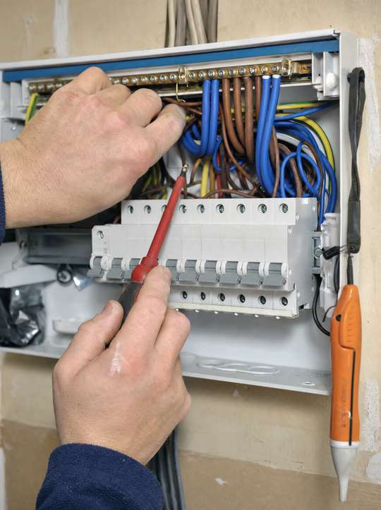 An electrician wiring a new consumer unit with coloured cables.
